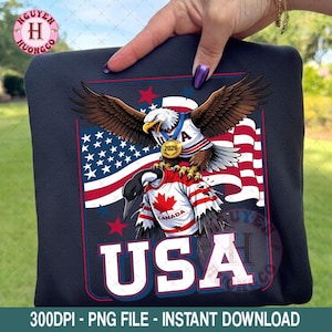 May include: A navy blue hoodie featuring a graphic of an eagle and a goose wearing jerseys, with the USA flag in the background. The word "USA" is displayed in white block letters. The image also includes the text "2026".