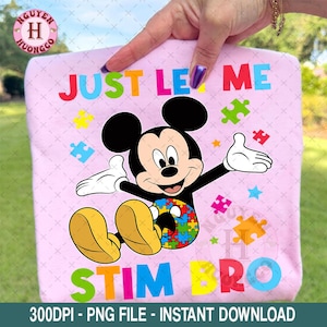 May include: A light pink t-shirt featuring Mickey Mouse with the text "JUST LET ME STIM BRO". Mickey Mouse is black, white, and yellow, with a puzzle piece design on his shorts. Colorful puzzle pieces and stars are scattered around the character.