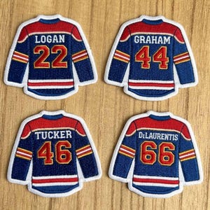 May include: Four embroidered hockey jersey patches. Each patch is blue with red and white accents. The patches display the names "Logan", "Graham", "Tucker", and "DiLaurentis" with the numbers 22, 44, 46, and 66.