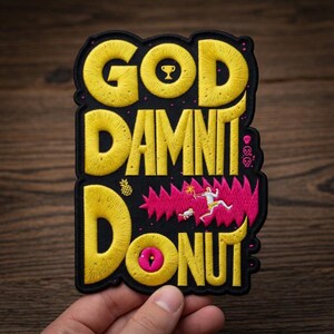 May include: Embroidered patch with the words "GOD DAMN DONUT" in yellow, with a trophy, pineapple, and cartoon figures. The patch has a black background with pink accents and a yellow donut.
