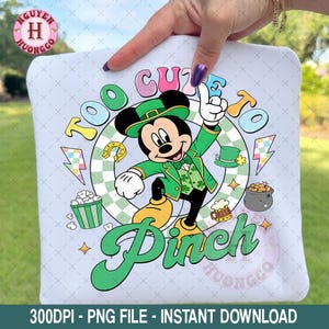 May include: A light blue graphic tee featuring Mickey Mouse in a green leprechaun outfit. The text reads "Too Cute To Pinch" in green. Other graphics include a horseshoe, pot of gold, and beer mug.