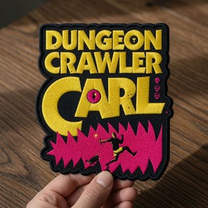May include: Embroidered patch featuring the text "DUNGEON CRAWLER CARL" in yellow thread on a black background. The word "CARL" is large and stylized. A pink jagged design and a small illustration of a person and dog are also included.