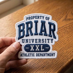 May include: A white embroidered patch with the text "PROPERTY OF BRIAR UNIVERSITY ATHLETIC DEPARTMENT". The word "BRIAR" is in large, navy blue letters. The patch also features the text "-XXL-".