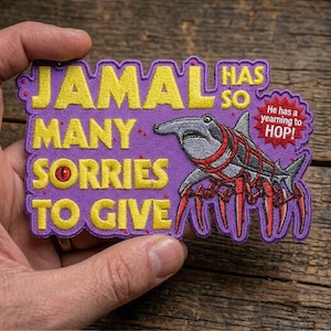 May include: A purple embroidered patch with yellow text that reads "JAMAL HAS SO MANY SORRIES TO GIVE." A hammerhead shark with red accents and spider-like legs is featured. A red burst bubble says "He has a yearning to HOP!"