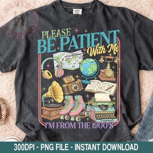 May include: Dark gray t-shirt with a vintage-themed graphic. The design includes the text "PLEASE BE PATIENT With Me I'M FROM THE 1900'S" along with illustrations of a globe, headphones, roller skates, and a typewriter.