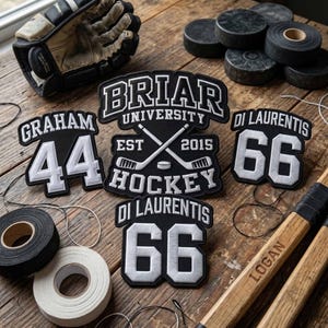 Puede incluir: Un conjunto de parches de hockey en blanco y negro, discos, cinta adhesiva y palos de hockey sobre una superficie de madera. Los parches muestran "Briar University Hockey" y nombres y números de jugadores. Un guante de hockey es visible.