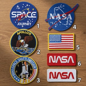 May include: A selection of seven embroidered patches featuring space and NASA designs. The patches display the NASA logo, an American flag, and text such as "SPACE JOURNEY" and "APOLLO 11". The patches are in various shapes and colours.