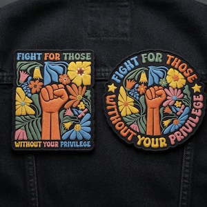 Könnte beinhalten: Zwei gestickte Aufnäher mit dem Text "FIGHT FOR THOSE WITHOUT YOUR PRIVILEGE". Einer ist quadratisch, der andere rund. Beide zeigen eine geballte Faust, Blumen und Blätter in Orange, Gelb, Blau und Rosa auf schwarzem Hintergrund.