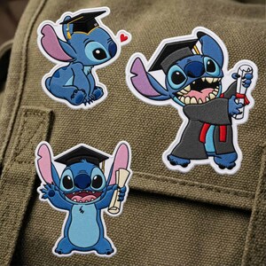 K&ouml;nnte beinhalten: Drei gestickte Aufn&auml;her mit der Figur Stitch aus Lilo & Stitch. Einer zeigt Stitch mit Abschlusskappe, ein anderer in einer Robe mit Diplom und der dritte mit Kappe und Diplom. Die Aufn&auml;her sind blau, schwarz und wei&szlig;.