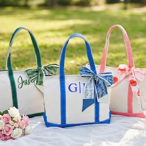 May include: Three canvas tote bags with colorful accents. One bag has green handles and trim, with the name "Jessica" embroidered in green. Another has blue handles and trim, with the initials "G|I" embroidered in blue. The third bag has pink handles and trim.