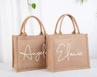 May include: Two brown burlap tote bags with white script lettering. The bag on the left says "Angela" and the bag on the right says "Elanie".