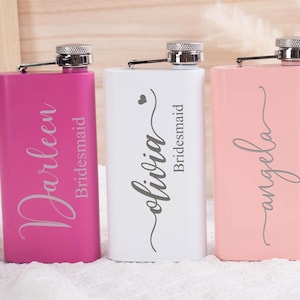 Könnte beinhalten: Drei personalisierte Flachmänner in Pink, Weiß und Pfirsich. Jeder Flachmann hat einen silbernen Deckel und ist mit einem Namen und dem Wort "Bridesmaid" graviert. Die Flachmänner sind rechteckig und stehen auf einer weißen Oberfläche.