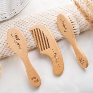 May include: Two light-colored wooden hairbrushes and one wooden comb. The first brush is engraved with the name Marcia and baby footprints. The comb is engraved with the name Lesley. The second brush is engraved with the name Nancy and a rocking horse.