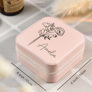 May include: A pink jewelry box with a zipper closure. The box is decorated with a floral design and the name "Amelia". The box measures 4 inches by 4 inches and 2 inches tall.