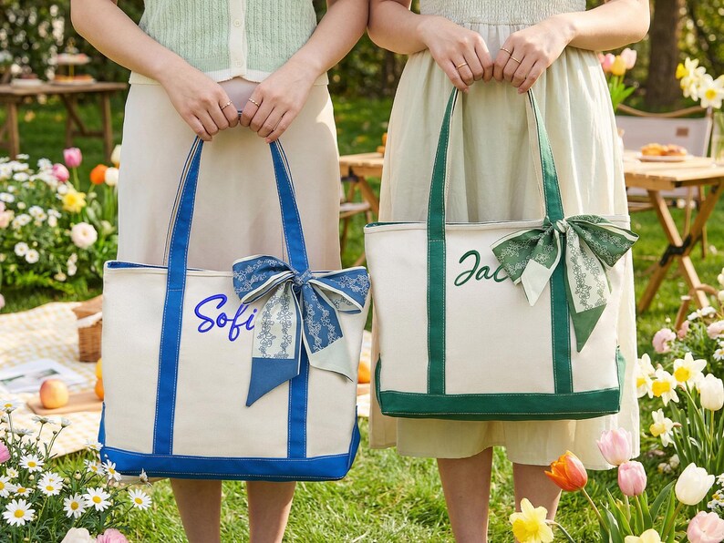 May include: Two canvas tote bags with personalized names. One bag is white with blue trim and the name "Sofi" in blue script, adorned with a blue bow. The other is white with green trim, the name "Jac" in green script, and a green bow.