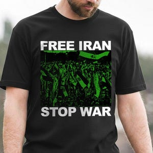 Op de afbeelding: Zwart t-shirt met de woorden "FREE IRAN STOP WAR" in witte blokletters. Het shirt heeft een groen-zwarte afbeelding van een menigte die vlaggen vasthoudt. Het shirt is gemaakt van een zacht materiaal.