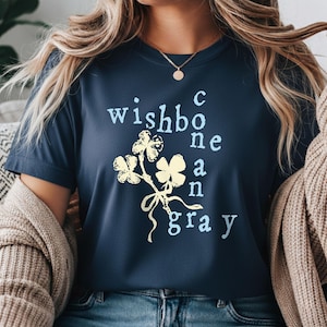 May include: Navy blue t-shirt with the text "wishbone and gray" in light blue, and a floral design in yellow. The shirt is a crew neck and is made of a soft material.