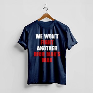 May include: Navy blue t-shirt with the text "WE WON'T FIGHT ANOTHER RICH MAN'S WAR" in white and red block letters. The shirt is hanging on a wooden hanger against a white background.