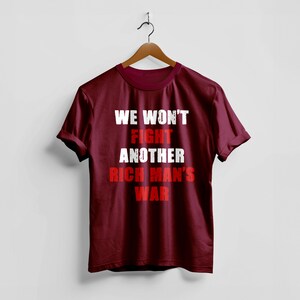 May include: A maroon t-shirt with the text "WE WON'T FIGHT ANOTHER RICH MAN'S WAR" in white and red block letters. The shirt is hanging on a wooden hanger against a white background.
