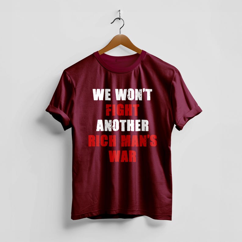 May include: A maroon t-shirt with the text "WE WON'T FIGHT ANOTHER RICH MAN'S WAR" in white and red block letters. The shirt is hanging on a wooden hanger against a white background.