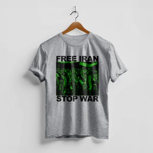 Op de afbeelding: Een grijs t-shirt met de tekst "FREE IRAN" boven een groen en zwarte afbeelding van een menigte met vlaggen. De woorden "STOP WAR" staan in het zwart onder de afbeelding.