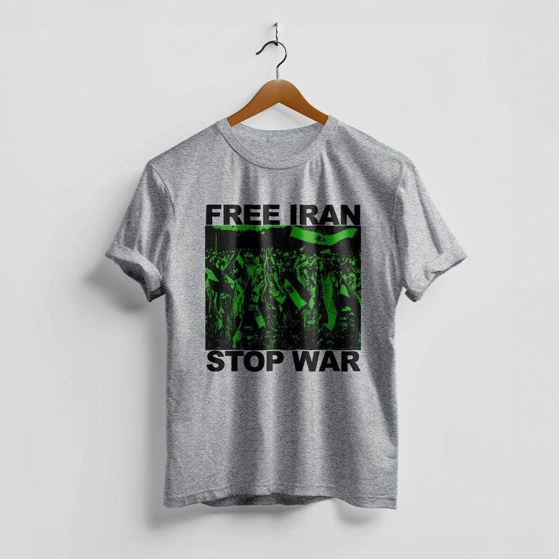 Op de afbeelding: Een grijs t-shirt met de tekst "FREE IRAN" boven een groen en zwarte afbeelding van een menigte met vlaggen. De woorden "STOP WAR" staan in het zwart onder de afbeelding.