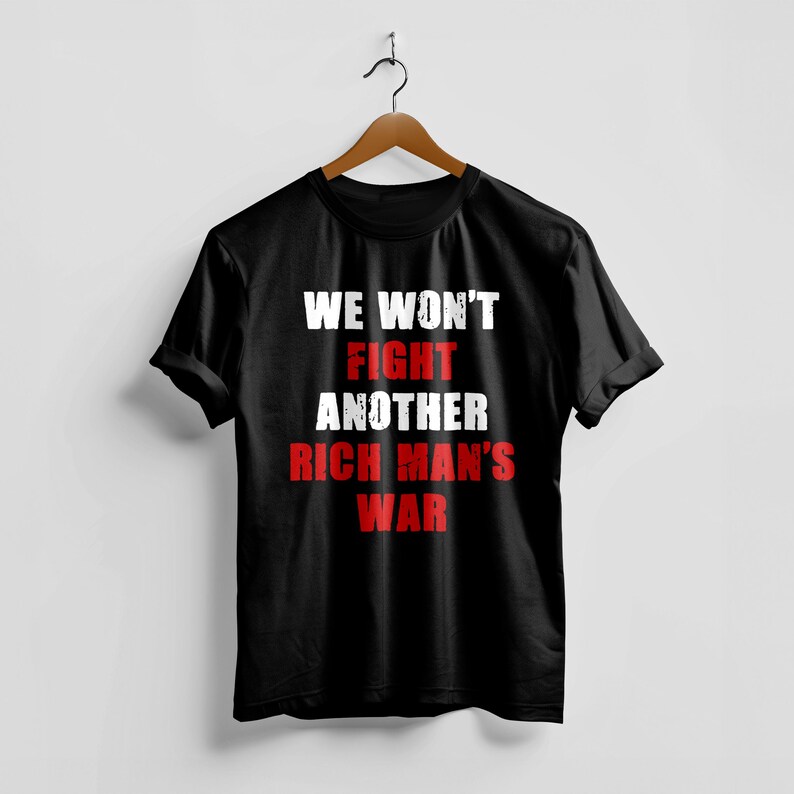 May include: Black t-shirt with the text "WE WON'T FIGHT ANOTHER RICH MAN'S WAR" in white and red lettering. The shirt is hanging on a wooden hanger against a white background.