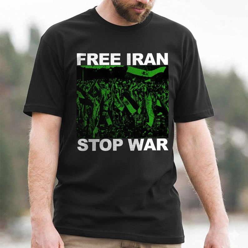 Op de afbeelding: Zwart t-shirt met de woorden "FREE IRAN STOP WAR" in witte blokletters. Het shirt heeft een groen-zwarte afbeelding van een menigte die vlaggen vasthoudt. Het shirt is gemaakt van een zacht materiaal.