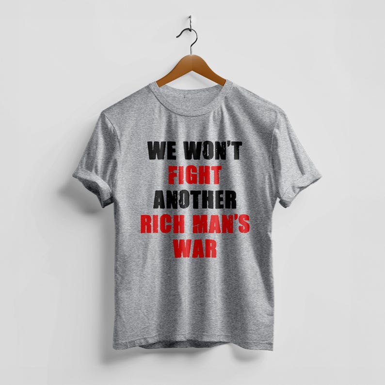 May include: A heather gray t-shirt with the text "WE WON'T FIGHT ANOTHER RICH MAN'S WAR" in black and red block letters. The shirt is hanging on a wooden hanger against a white background.