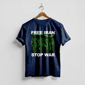 Op de afbeelding: Marineblauw t-shirt met de witte tekst "FREE IRAN STOP WAR". De afbeelding in het midden toont een groen-zwarte afbeelding van een menigte die vlaggen vasthoudt. Het t-shirt hangt aan een houten hanger.