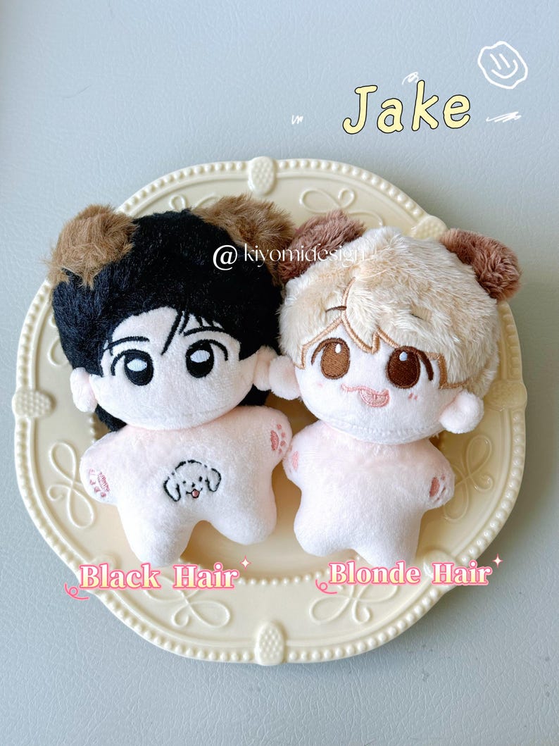 May include: Two plush dolls with cartoon faces and fluffy hair, one with black hair and the other with blonde hair, are displayed on a decorative plate. The dolls have pink bodies and embroidered facial features. Text on the plate reads "Black Hair" and "Blonde Hair".