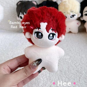 May include: A plush doll with red hair and large eyes is held by a hand. The doll has a white body and is surrounded by other similar dolls. Text on the image reads "Bambi eyes Red hair" and "Hee". The doll is a cute, handmade item.