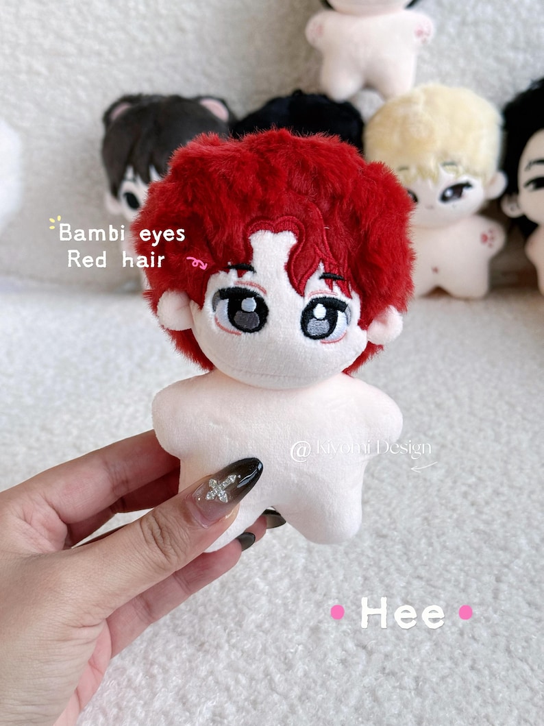 May include: A plush doll with red hair and large eyes is held by a hand. The doll has a white body and is surrounded by other similar dolls. Text on the image reads "Bambi eyes Red hair" and "Hee". The doll is a cute, handmade item.
