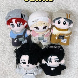 May include: Five doll outfits are displayed, each with a unique style. The dolls wear beanies, overalls, and hoodies in various colors, including gray, white, and black. The word "Outfits" is written in yellow. The text "The clothes might be too big for Niki doll Because his body is smaller" is also visible.