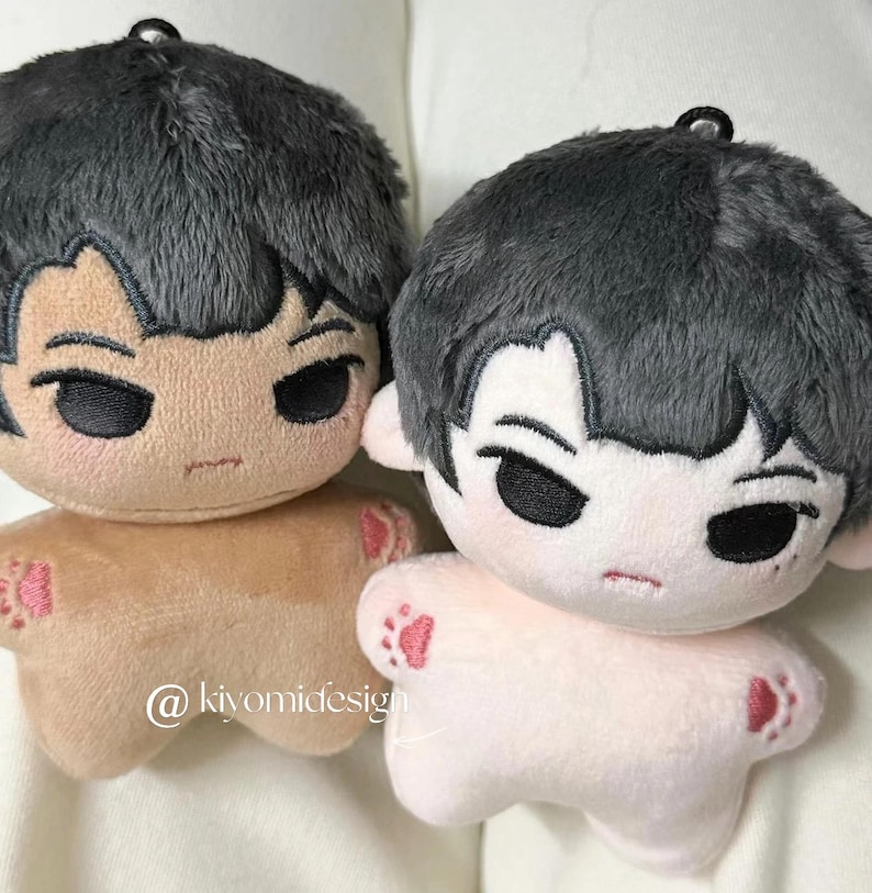 May include: Two plush dolls with gray hair and stern facial expressions. One doll is tan, the other is light pink. Both have small red paw prints on their feet. The dolls have a black loop at the top for hanging.