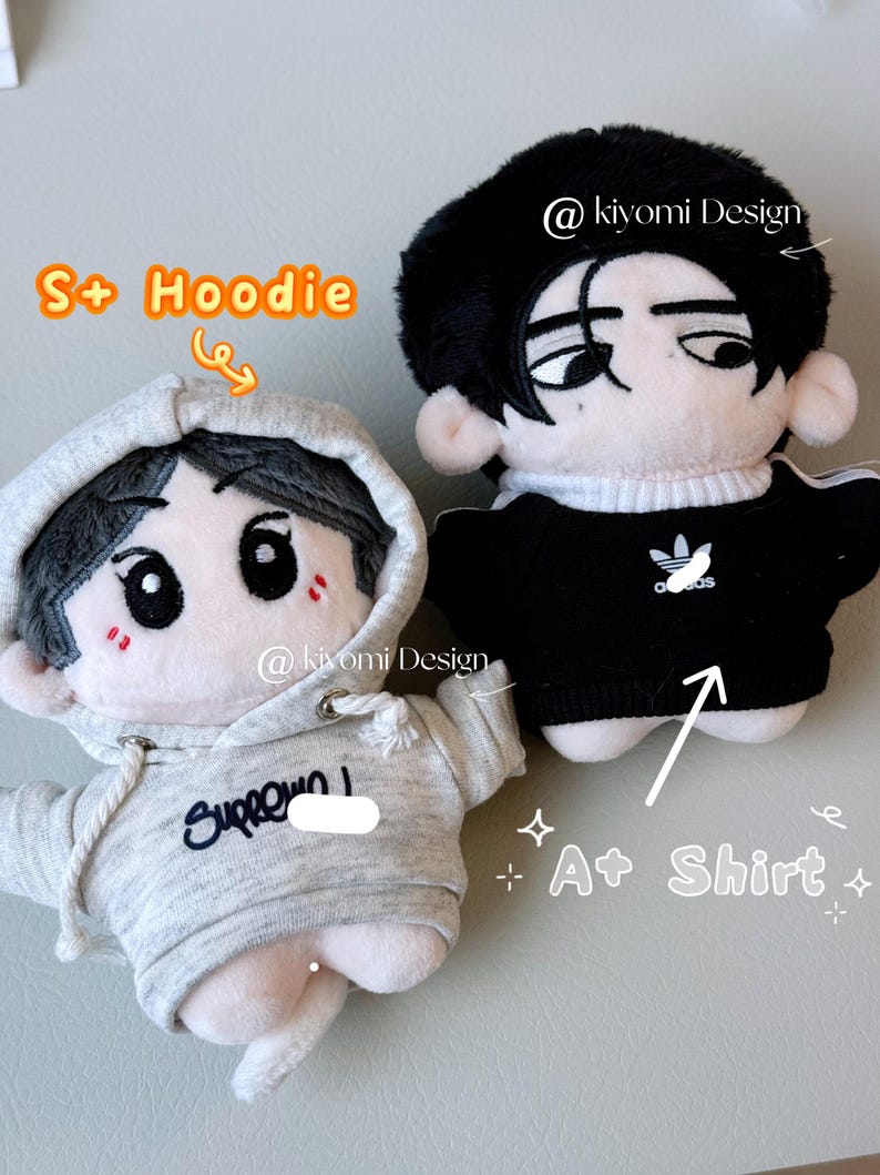 May include: Two plush dolls, one in a gray hoodie with the text "Supreme" and the other in a black shirt with a white logo. Both dolls have black hair and cartoon-style faces. The text "S+ Hoodie" and "A+ Shirt" are also visible.