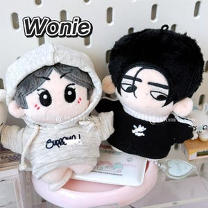 May include: Two plush dolls with embroidered facial features and clothing. One doll wears a gray hoodie with the word "Superown" and the other wears a black shirt with white stripes and a logo. The word "Wonie" is at the top.