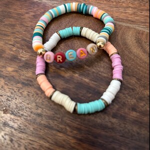 May include: Two colorful beaded bracelets, one with a multi-colored pattern and the other with the word "DREAM" spelled out in colorful letters.