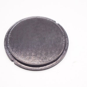 May include: A black plastic lens cap for a camera.