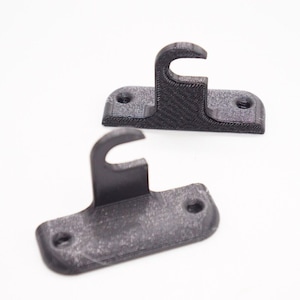 May include: Two black plastic wall mounts with a hook on each. The hooks are designed to hold a curtain rod.