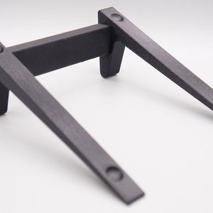 May include: A black metal shelf bracket with a rectangular support and two angled arms. The bracket has pre-drilled holes for mounting and is designed to support a shelf. The bracket is made of a durable material and is suitable for various applications.