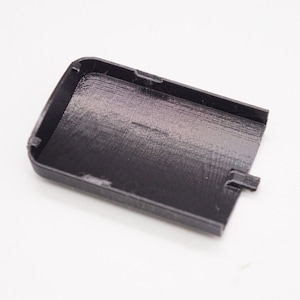 May include: A black plastic case with a smooth, textured surface. The case has a small opening on one side.