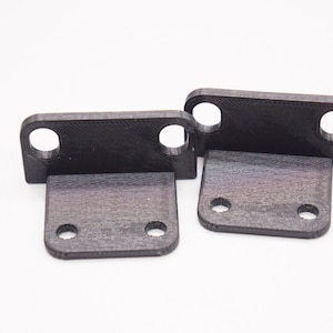 Puede incluir: Dos soportes de plástico negro con cuatro agujeros cada uno. Los soportes están inclinados y tienen una superficie texturizada.