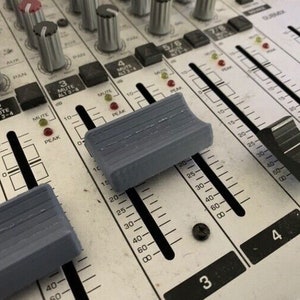 May include: Close-up of a silver mixing board with two gray faders and the numbers 3, 4, and 5/6 printed on the board.