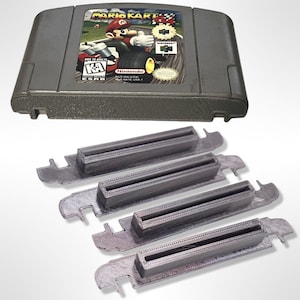Puede incluir: Un cartucho de juego gris de Nintendo 64 para Mario Kart 64. El cartucho se muestra con cuatro ranuras de cartucho de plástico gris.