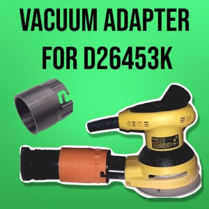 Puede incluir: Un adaptador de aspiradora negro para una lijadora D26453K. El adaptador es un anillo de plástico con un agujero en el centro. La lijadora es amarilla y negra y tiene un puerto de recolección de polvo.