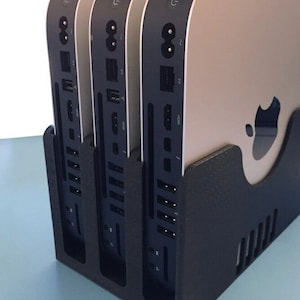 Może przedstawiać: Trzy srebrne komputery Mac mini ułożone pionowo w czarnym stojaku. Widoczna jest tylna część komputerów, z portami i połączeniami.