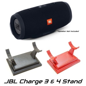 May include: A black JBL Charge 3 or 4 speaker with an orange logo, and two stands, one gray and one red. The stands are designed to hold the speaker. The text "JBL Charge 3 & 4 Stand" is at the bottom.