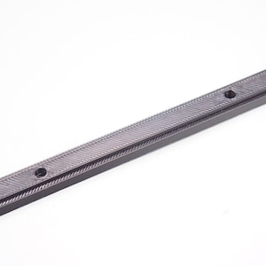 May include: A dark gray, rectangular object with a textured, diagonal pattern. The object has two circular holes and is approximately 12 inches long. The item appears to be made of a solid, possibly metal, material.