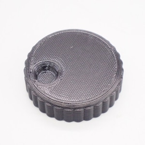 May include: A black plastic knob with a textured surface and a circular hole in the centre.